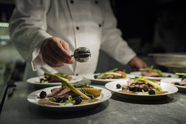 Chef preparing a dish of venison with apple and seasonal vegetables.