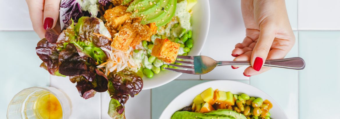 Woman eating a vegan salad bowl with tofu, avocado and edamame at the restaurant