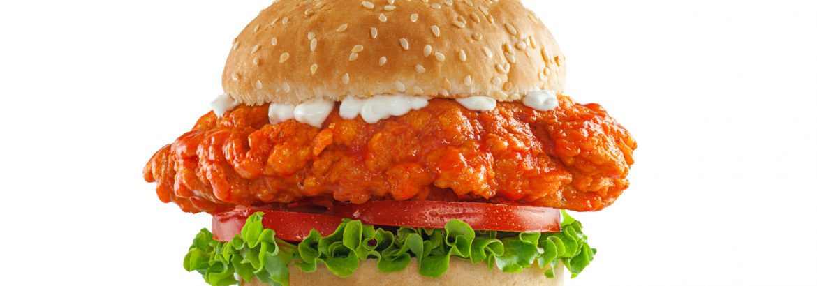 High resolution, digital capture of a spicy Buffalo chicken sandwich with lettuce, tomatoes, and bleu cheese dressing, on a fresh sesame seed bun, set against a clean, white background sweep. Shot in an aspirational advertising style.