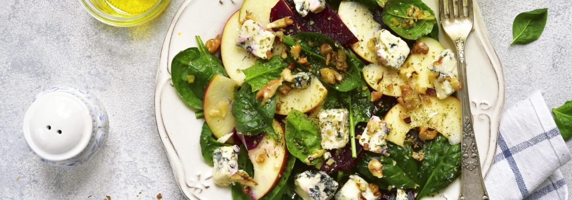 Autumn beet root salad with blue cheese,apple,,spinach and walnut on a vintage plate over light slate,stone or concrete background.Top view.