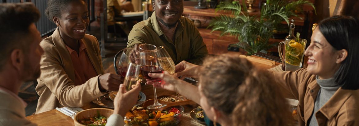 Diverse group of people clinking glasses while enjoying dinner party with friends and family in cozy interior